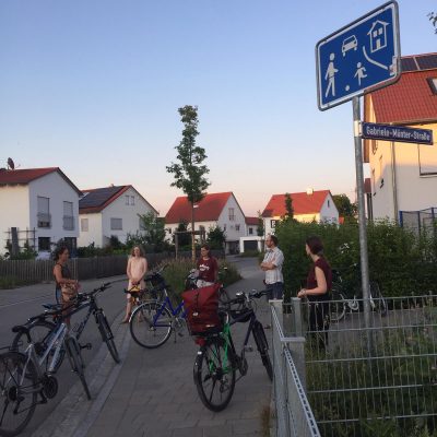 Menschen mit Fahrrädern an einer Kreuzung in einem Neubaugebiet. Daneben ein Straßenschild mit dem Namen Gabriele-Münter-Straße