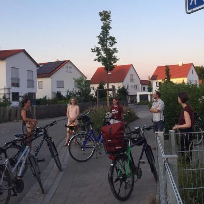 Menschen mit Fahrrädern an einer Kreuzung in einem Neubaugebiet. Daneben ein Straßenschild mit dem Namen Gabriele-Münter-Straße