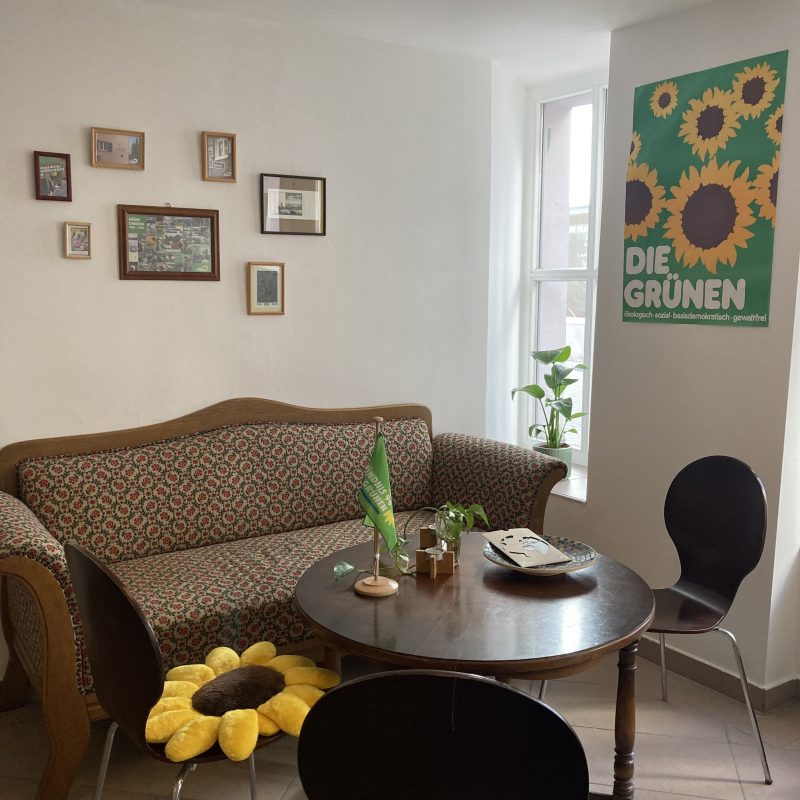 Couch mit Bilderrahmen darüber, Poster mit Sonnenblumen, Tisch mit Stühlen darum