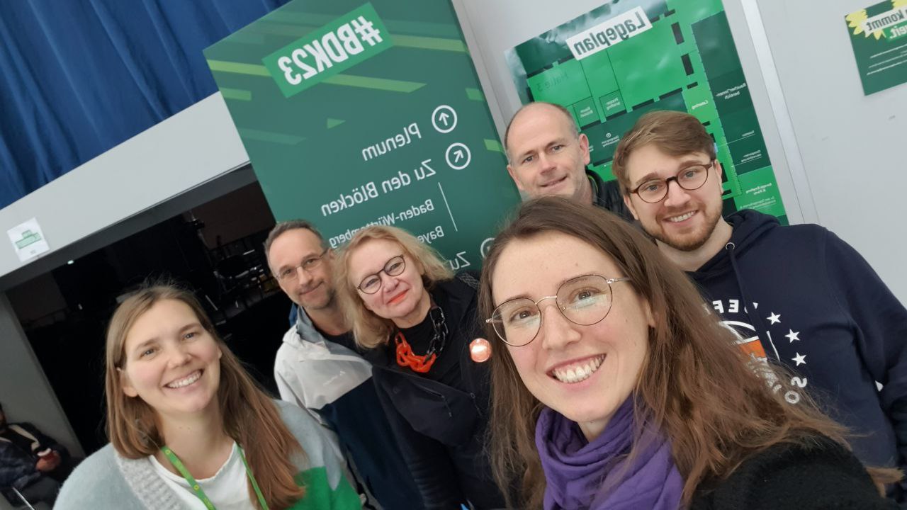 Eine Gruppe Menschen lächelt in die Kamera. Sie stehen vor einem grünen Aufsteller in der Kongresshalle Karlsruhe.
