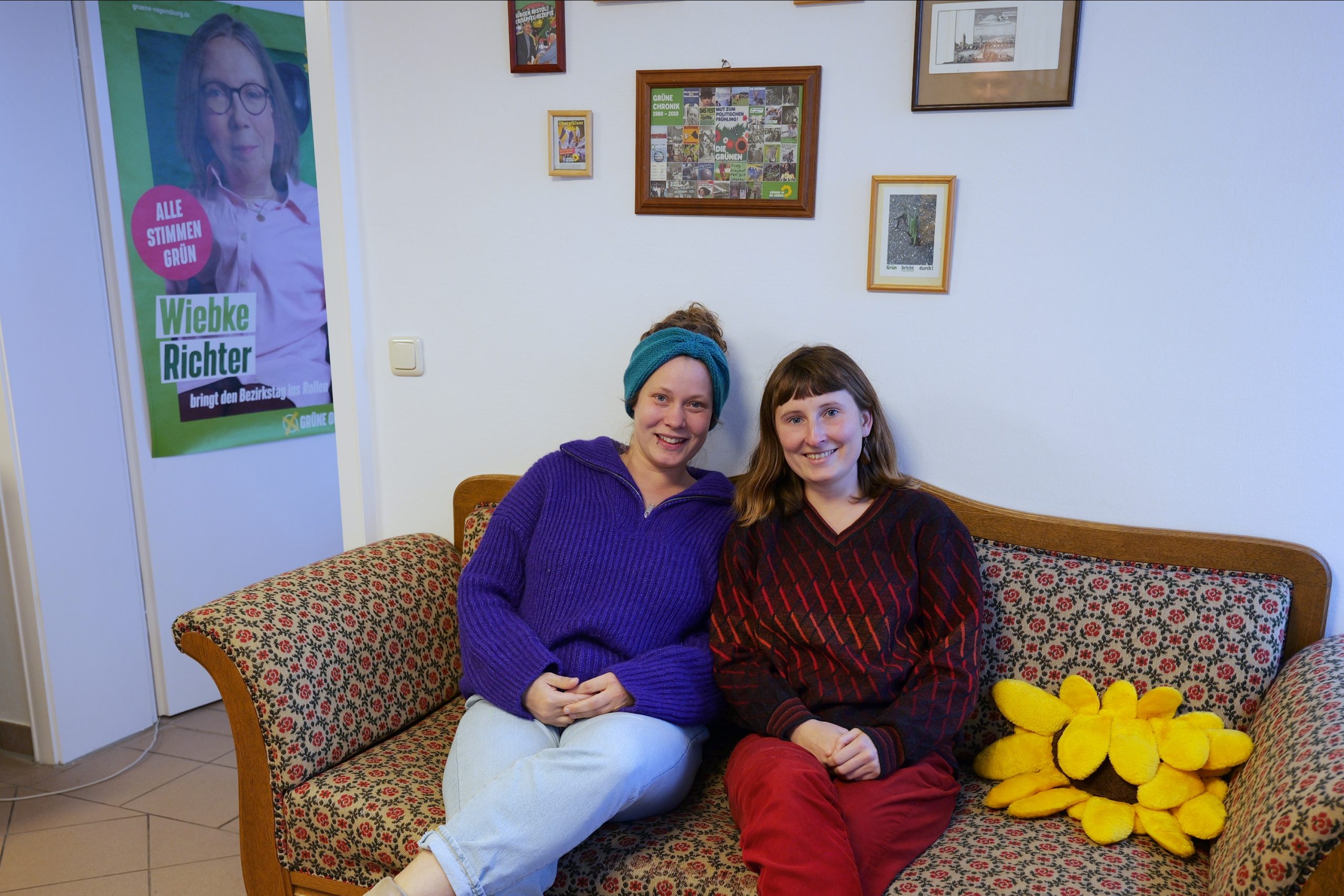 Yasmin Hopp und Annemarie Bruckert sitzen nebeneinander auf dem Sofa im Grünen Büro und lächeln in die Kamera.